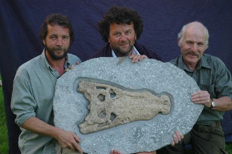 3 men holding up a fossil